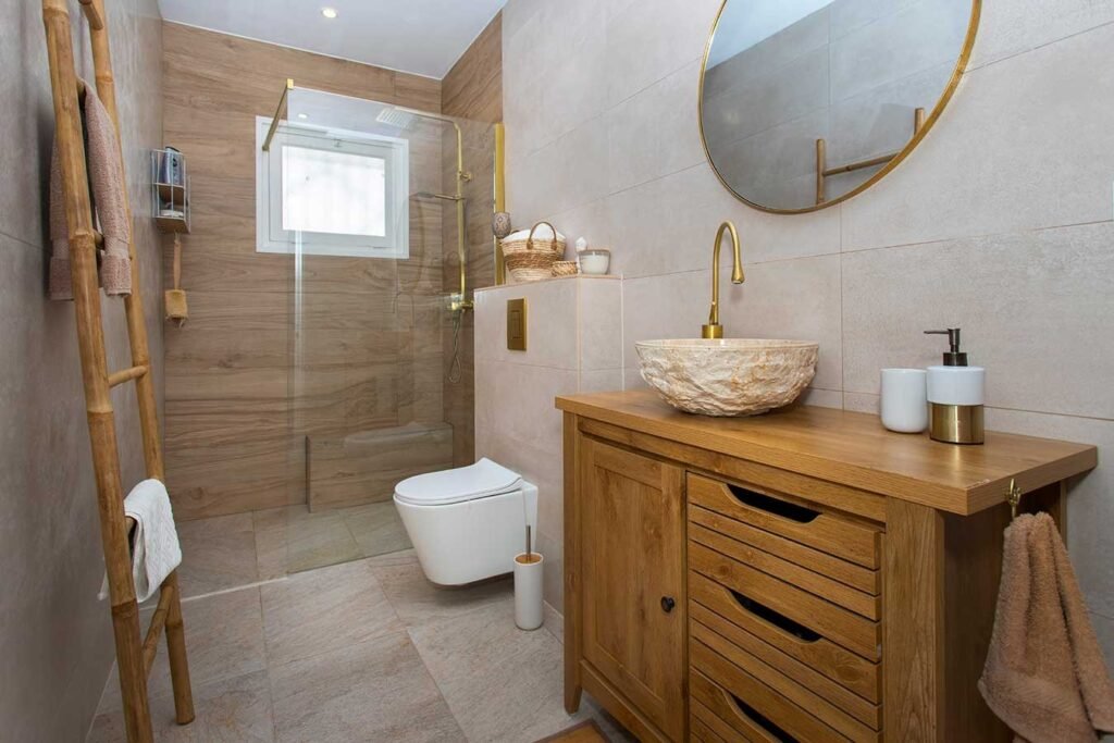 Fotografía profesional de un aseo de estilo rústico con un mueble de baño de madera natural, lavabo sobre encimera de piedra y espejo redondo