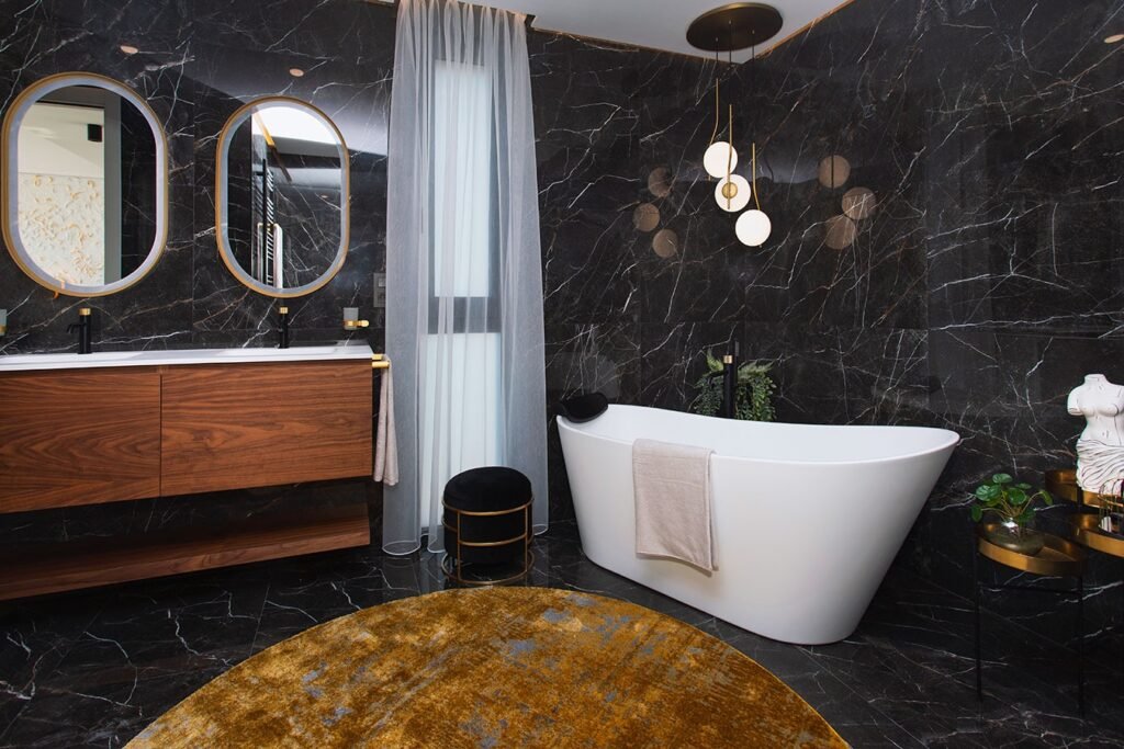 Fotografía de arquitectura interior de un baño sofisticado con paredes de azulejos negros, lavabo doble y espejos retroiluminados