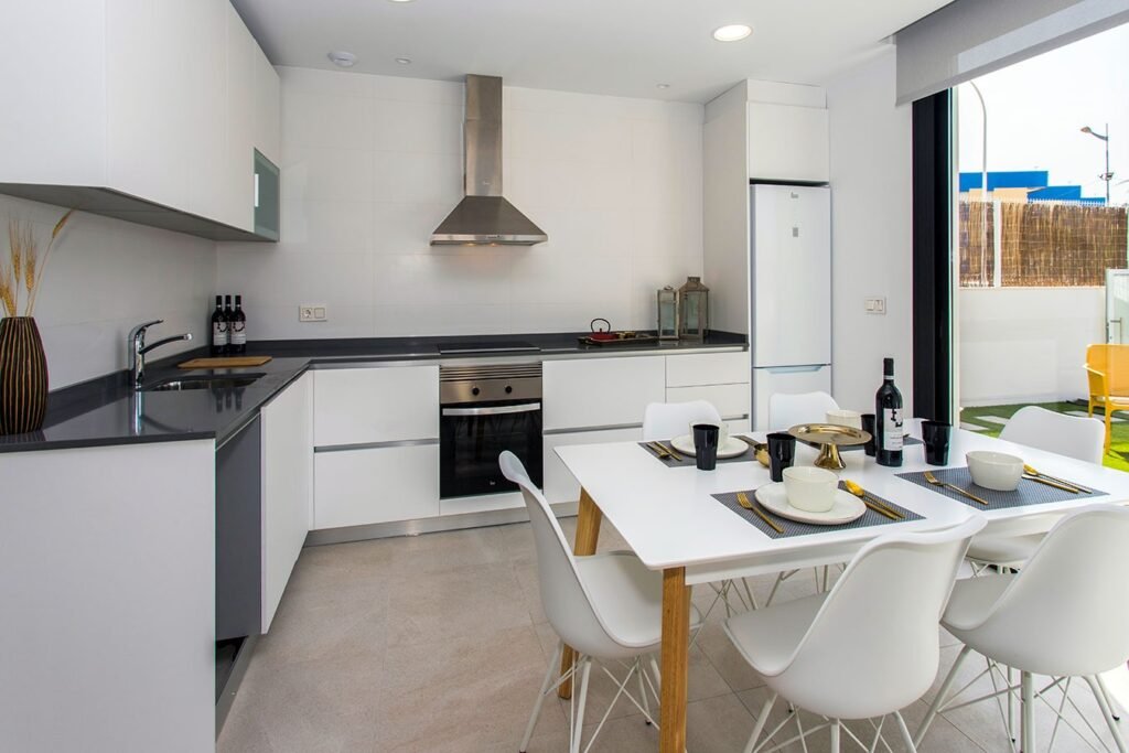 Fotografía profesional de una cocina moderna blanca con isla central, taburetes de diseño y electrodomésticos de acero inoxidable