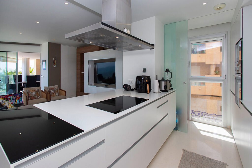 Contraste moderno en diseño de interiores con una cocina con armarios inferiores negros, encimeras blancas e imponentes cristaleras hacia el jardín