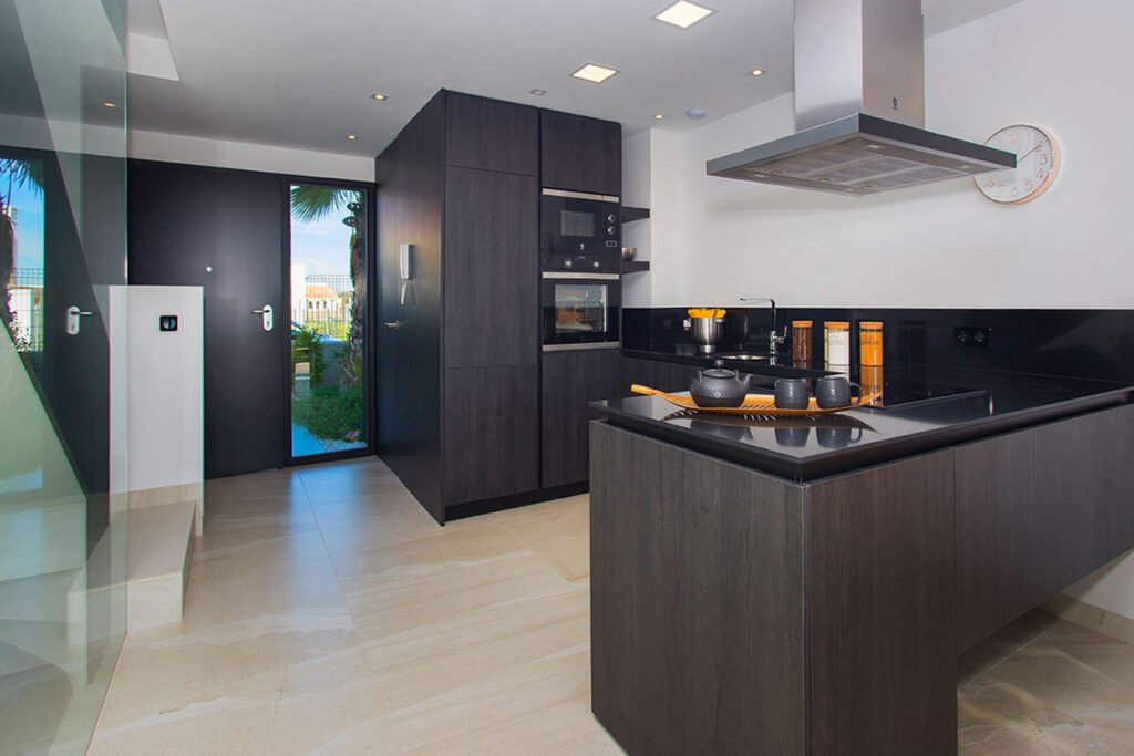 Interiorismo de cocina abierta con muebles oscuros texturizados, isla de trabajo espaciosa y campana extractora de acero de estética industrial
