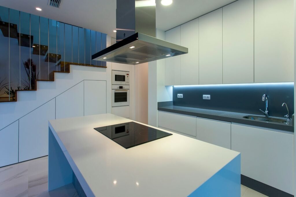 Interiorismo de una cocina minimalista de líneas puras con frentes blancos sin tiradores y vista hacia una escalera integrada al fondo