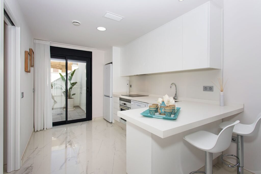 Solución de espacio en cocina alargada blanca, equipada con una isla central multifuncional y una iluminación técnica perfectamente distribuida