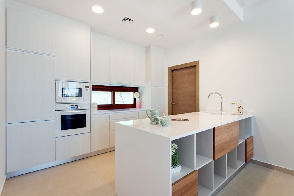 Simetría y orden en cocina moderna blanca con armarios empotrados hasta el techo, isla minimalista y juego de focos LED empotrados