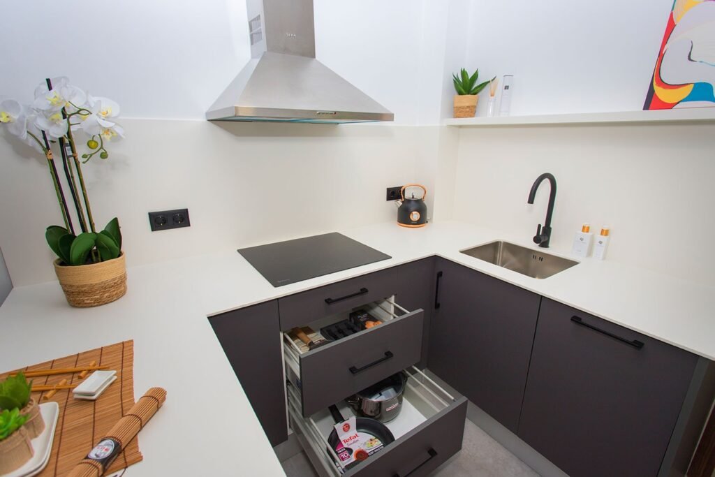 Aprovechamiento del espacio en cocina reformada con diseño en U, muebles blancos lacados, encimera oscura en contraste y accesorios de diseño