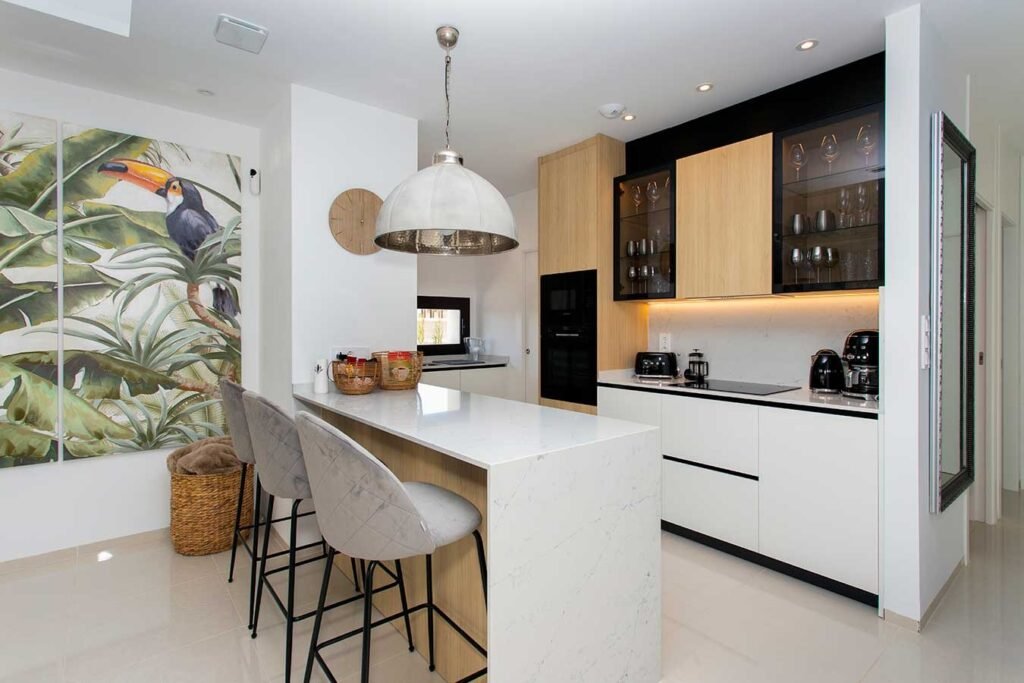 Proyecto de cocina muy luminosa de estilo nórdico que combina madera clara, mobiliario blanco, taburetes altos y plantas decorativas