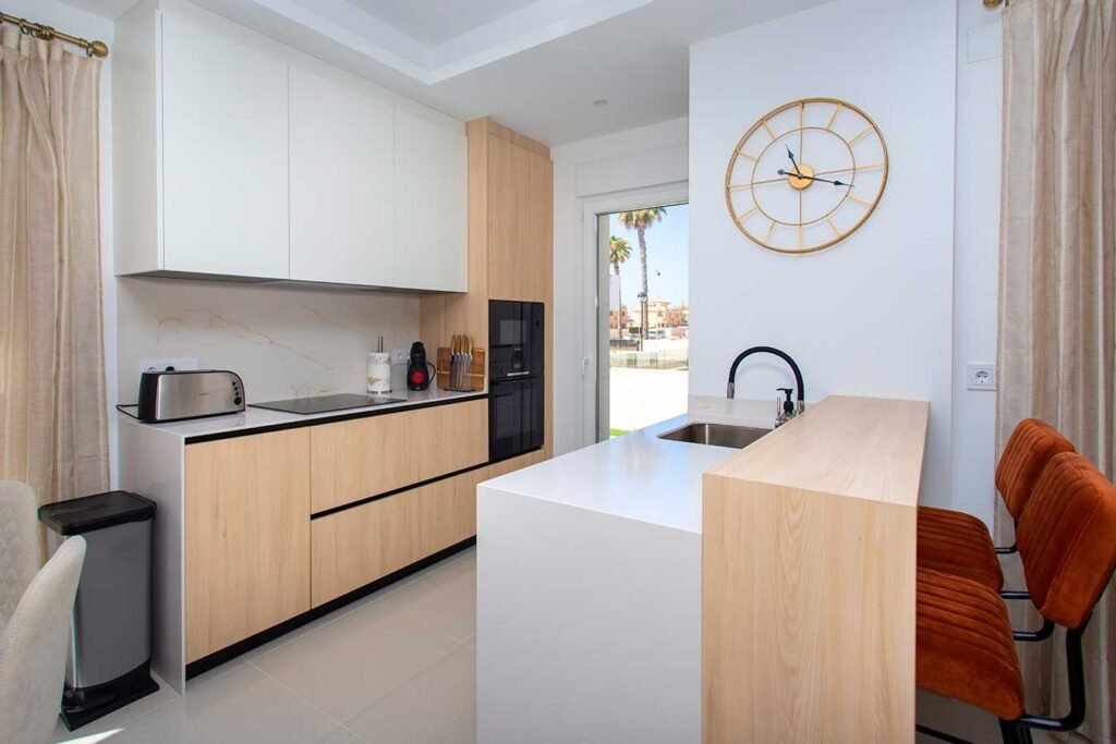 Reportaje fotográfico de una cocina minimalista blanca con isla central, grifería negra de diseño y un espacio diáfano muy elegante