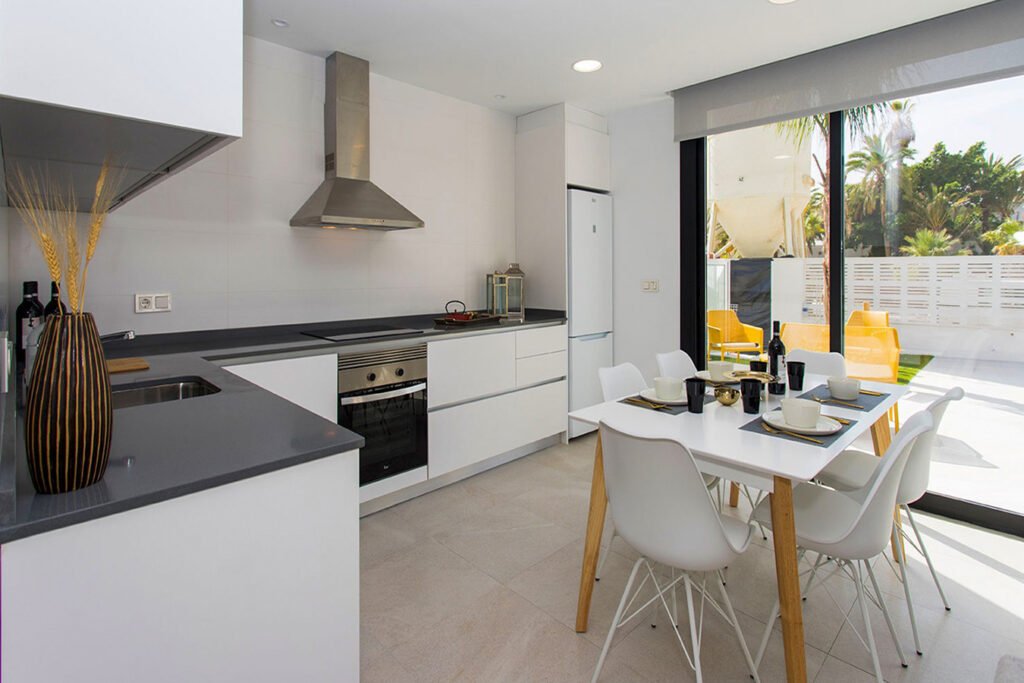 Cocina de diseño moderna en color blanco, inundada de luz natural gracias a un gran ventanal con vistas al exterior y suelo porcelánico claro