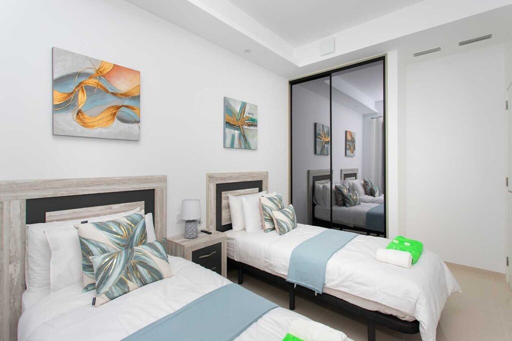 Distribución de espacio en un dormitorio juvenil con dos camas alineadas, armario empotrado con espejos y ambiente muy luminoso