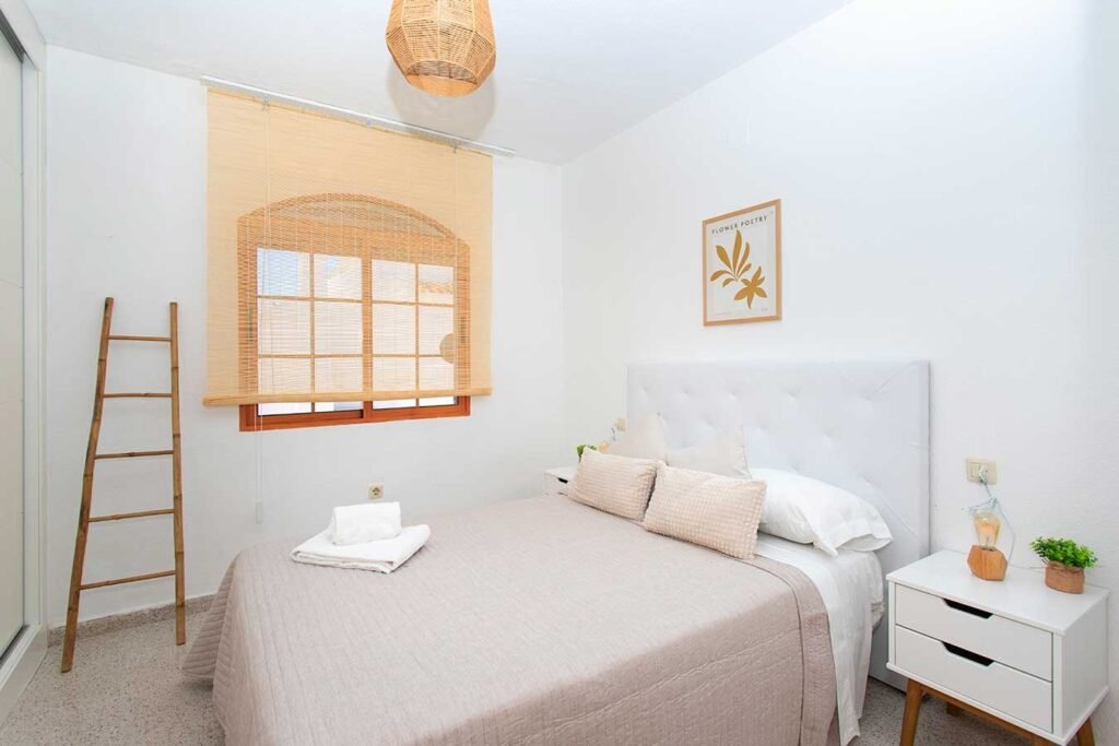 Habitación de matrimonio acogedora con paredes blancas, detalles de decoración rústica como una escalera de madera y ventana al fondo