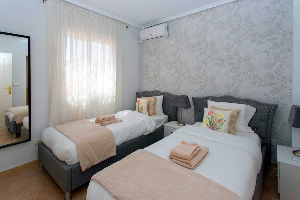 Fotografía técnica de un dormitorio de invitados alargado bien optimizado, con dos camas individuales vestidas con mantas beige