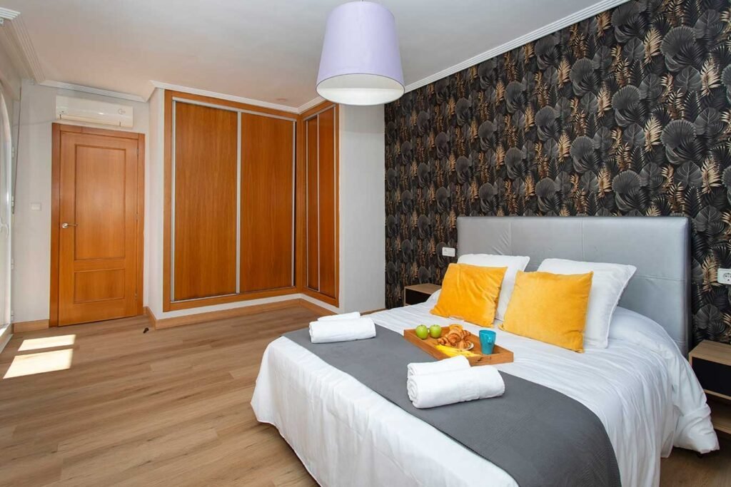 Diseño de interiores atrevido en un dormitorio que combina una pared de fondo oscura decorada, armarios de madera y cama perfectamente vestida