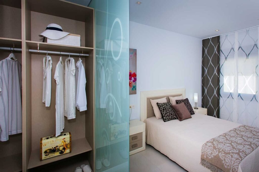 Vista de un dormitorio contemporáneo iluminado que cuenta con un armario vestidor integrado con puertas de cristal