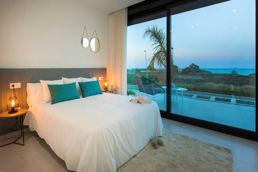 Reportaje de fotografía inmobiliaria de un dormitorio principal de lujo con gran cristalera y vistas a una piscina y al mar