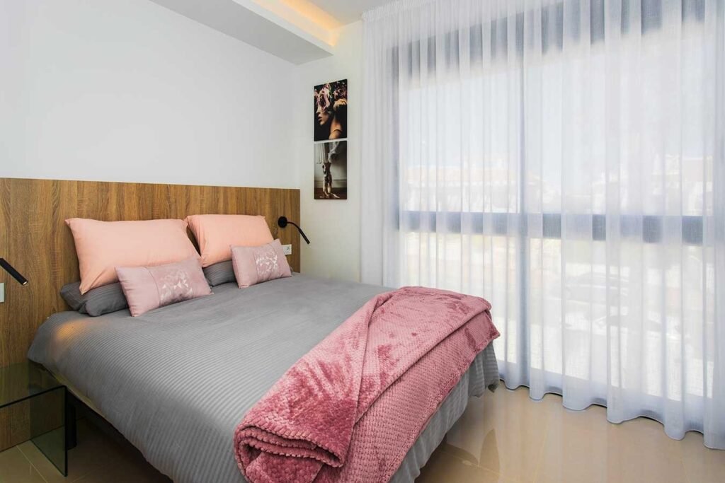 Decoración de dormitorio principal de estilo nórdico con textiles grises y rosados, cabecero de madera y luz natural templada
