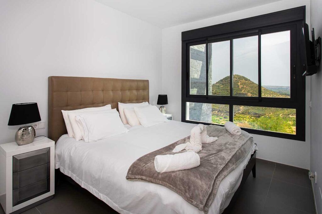 Fotografía de arquitectura interior de una habitación minimalista con cama de matrimonio espaciosa y vistas despejadas a través de un ventanal negro