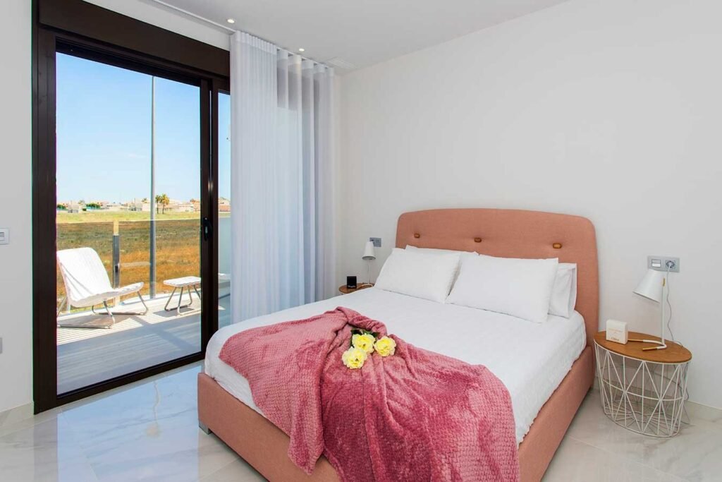 Interiorismo de dormitorio moderno que destaca por una estructura de cama estilo balinesa en tonos madera y manta rosa decorativa