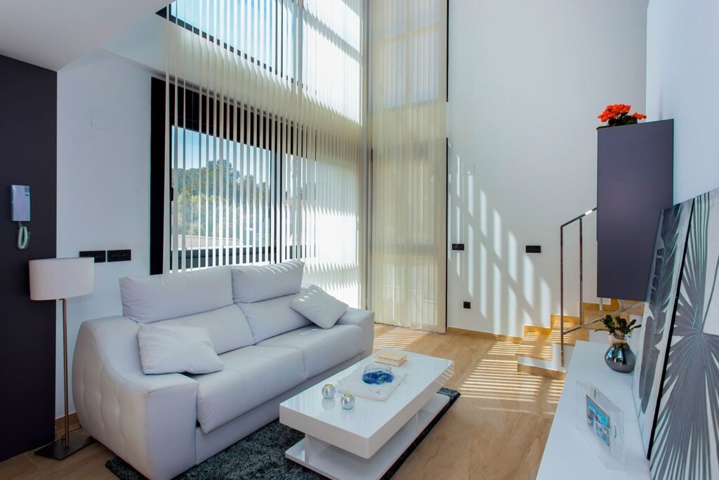 Salón de vivienda tipo dúplex con techos de doble altura, grandes ventanales y muebles en tonos blancos y grises