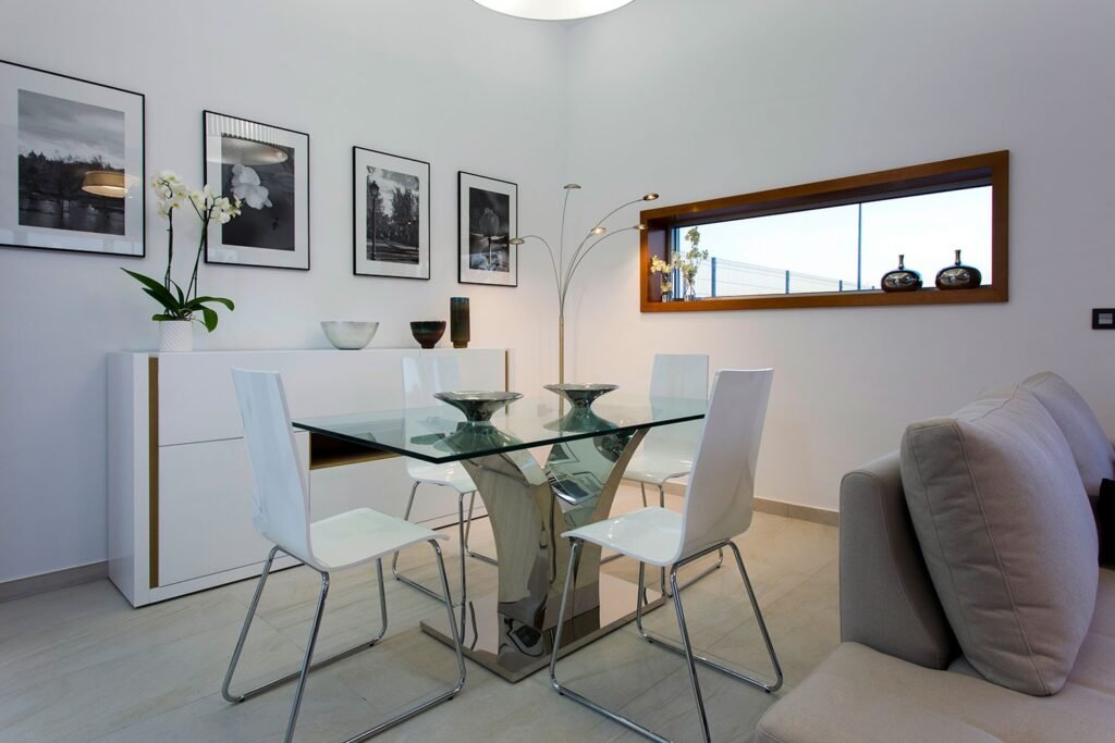 Zona de comedor moderna con mesa lacada en blanco, sillas minimalistas y galería de cuadros con marcos negros en la pared