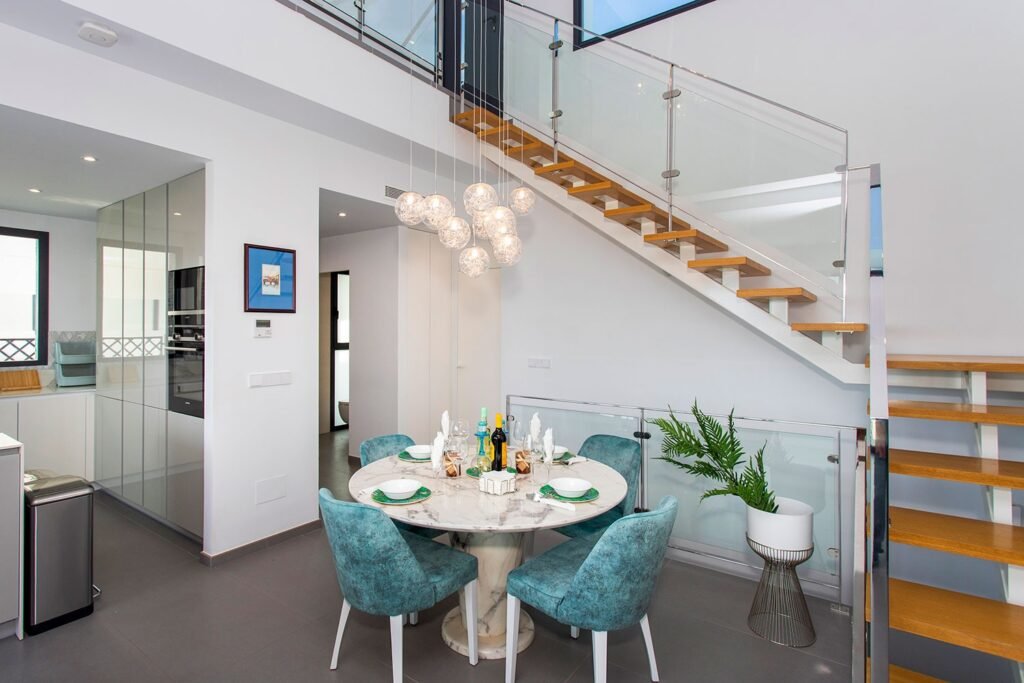 Fotografía inmobiliaria de planta baja abierta con salón, cocina al fondo y una moderna escalera de estructura vista