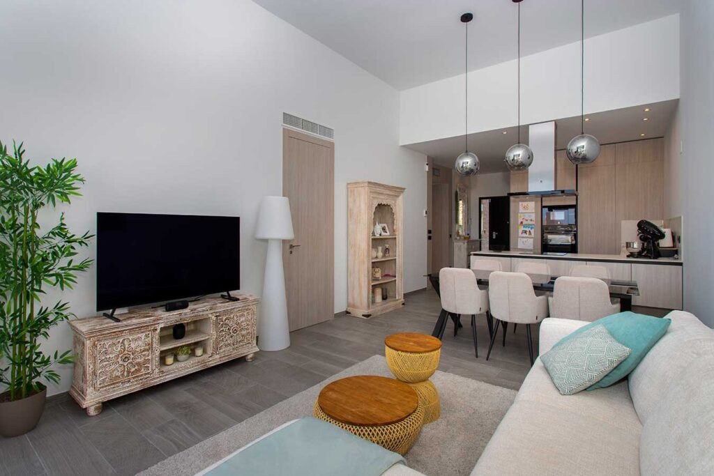 Fotografía inmobiliaria de salón diáfano de estilo nórdico comunicado con cocina blanca de diseño y taburetes