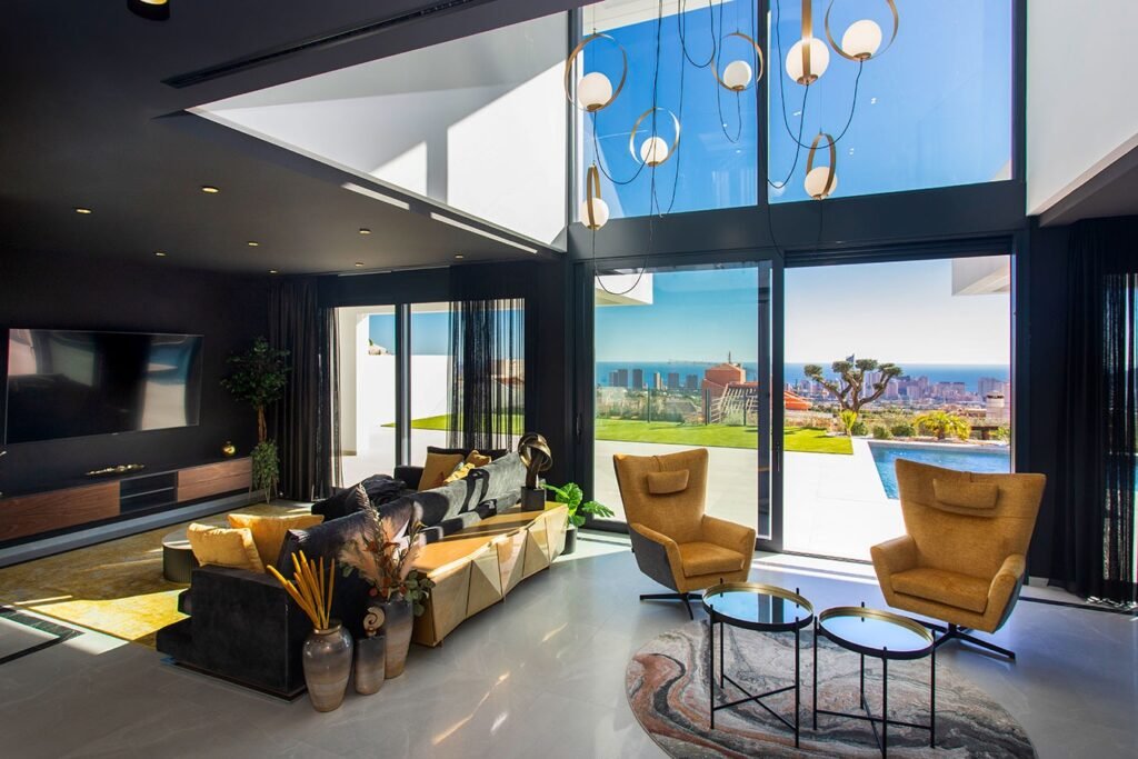 Impresionante salón de chalet de lujo con sofás de diseño, grandes cristaleras con vistas al mar y chimenea moderna