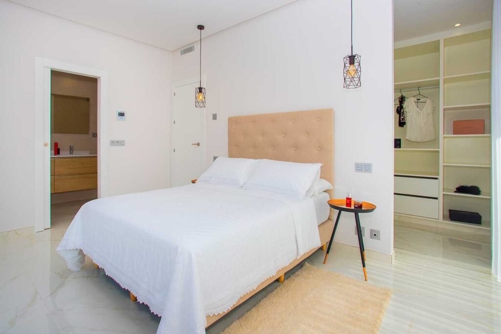 Fotografía de interiores de un dormitorio principal estilo suite en tonos claros con un armario vestidor empotrado al fondo