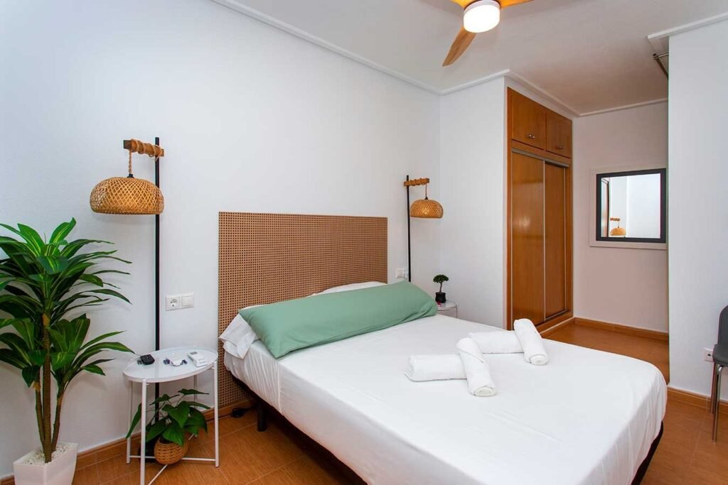 Vista de un dormitorio con cama de matrimonio, iluminación cálida de lectura y acabados en madera natural