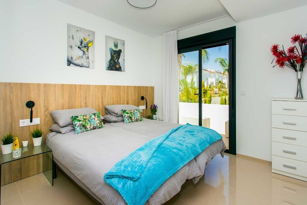 Espacioso dormitorio principal con cama grande decorada en tonos azules y un gran ventanal con vistas al jardín exterior