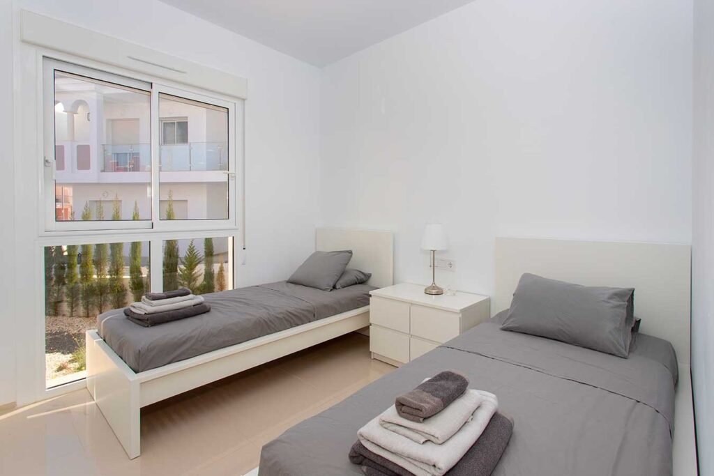 Optimización de espacio en un dormitorio de invitados alargado con dos camas en paralelo y ventana lateral con luz natural
