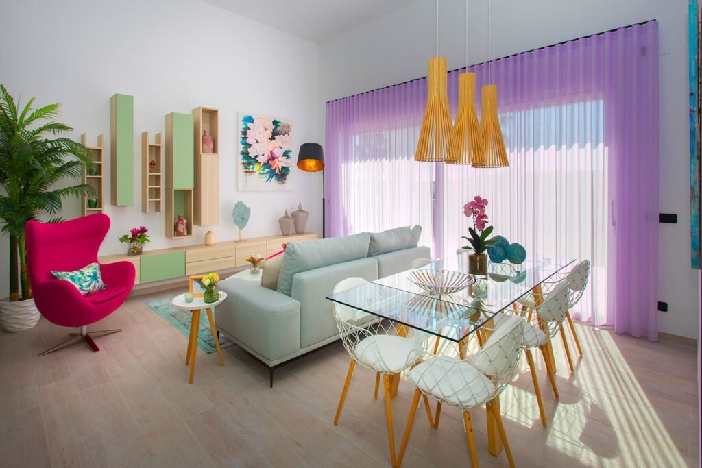 Fotografía profesional de un salón comedor moderno con mesa de cristal, sillas blancas y un sillón rosa de diseño en esquina luminosa