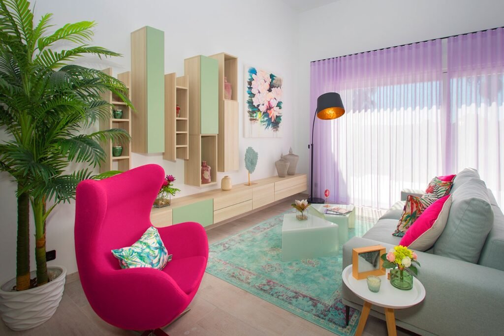 Diseño de interiores en un salón moderno con un llamativo sillón fucsia, alfombra estampada en tonos verdes y mueble de televisión de madera