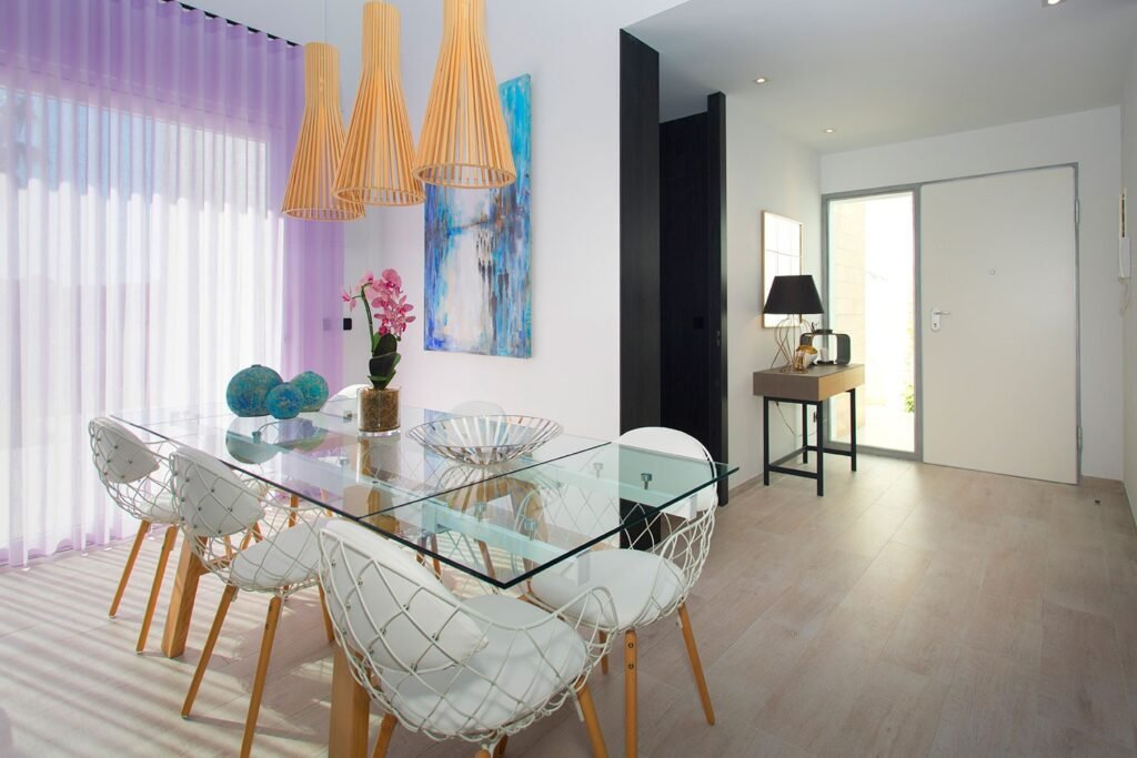 Amplio salón comedor de concepto abierto integrado con cocina, suelo de tarima clara, gran mesa de cristal y lámparas colgantes modernas