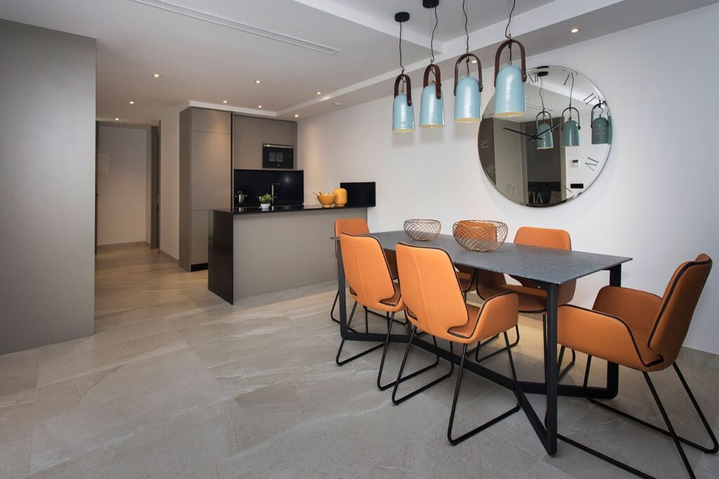 Vista de un salón comedor conectado con una cocina americana moderna en color gris oscuro, con sillas tapizadas en color naranja texturizado