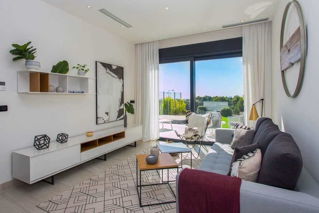Diseño de un salón contemporáneo con mueble bajo blanco para la televisión, decoración minimalista y gran cristalera con vistas a zonas verdes exteriores