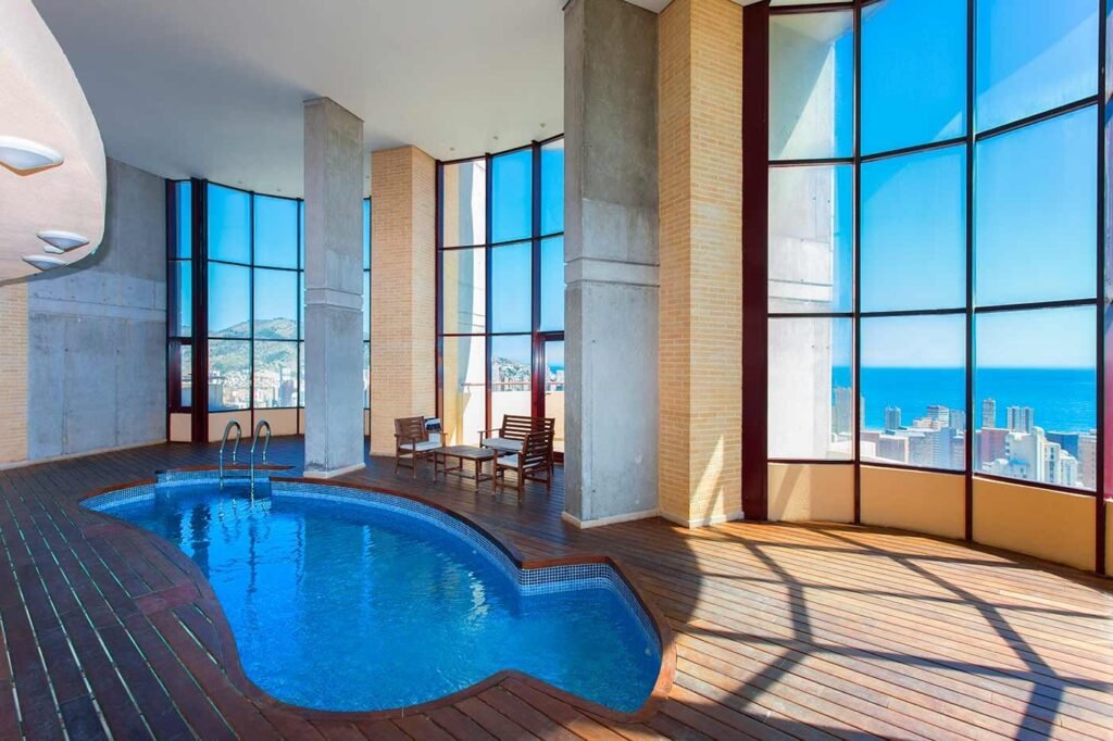Piscina interior climatizada con grandes columnas y ventanales acristalados hacia el exterior