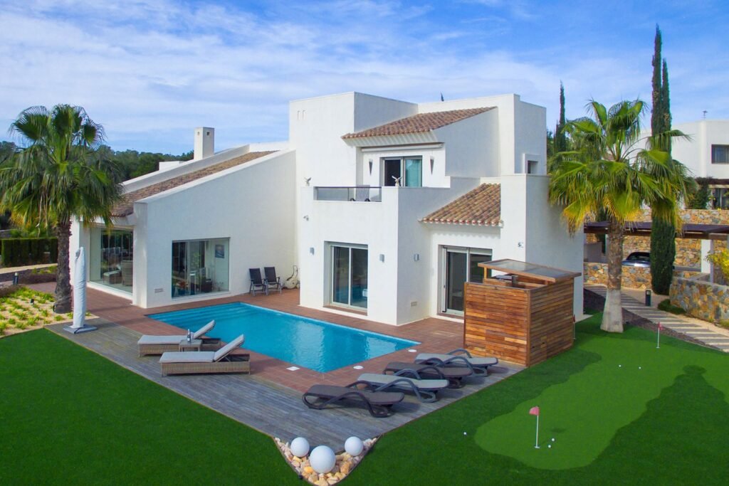 Parcela exterior con chalet moderno blanco, porche, piscina rectangular y jardín lateral