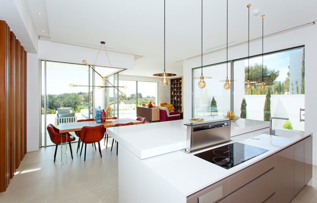 Cocina moderna con isla central blanca integrada con comedor y salón illumina