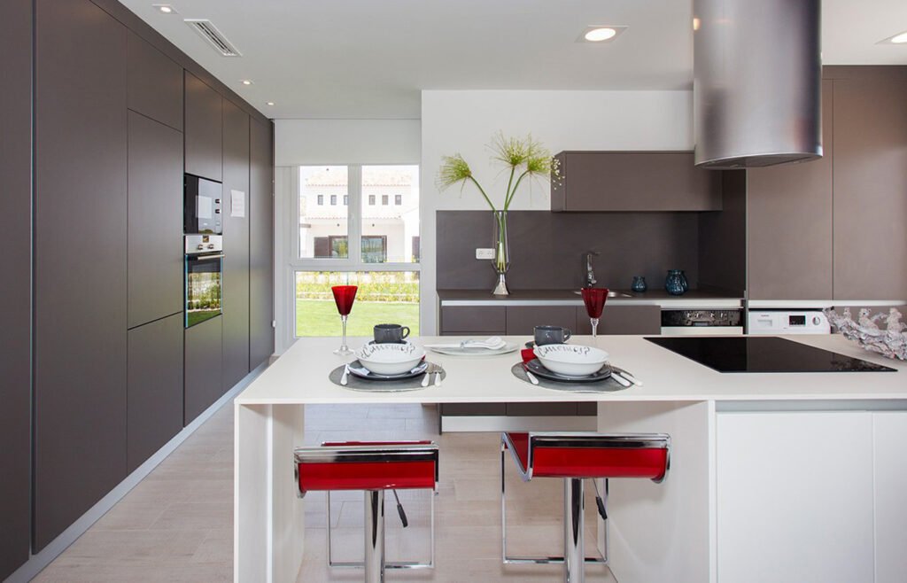 Cocina moderna alargada con barra, taburetes rojos y muebles oscuros
