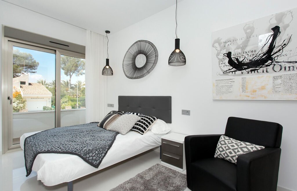 Dormitorio de matrimonio con cama hecha, lámparas colgantes y sillón negro